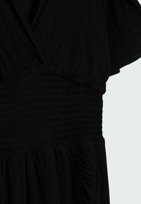 Musta mekko, jossa on V-painike, lyhyet hihat ja leveä rypistetty elastinen vyötärö yksinkertaisella vaalealla taustalla.