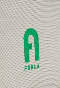 Logo ricamato su un tessuto crema chiaro testurizzato; presenta una prominente "F" verde sopra "FURLA" in un font verde abbinato.