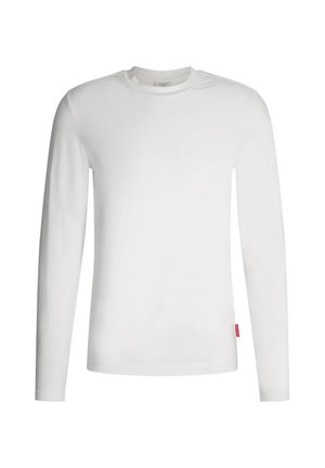 Chemise blanche à manches longues en coton doux, avec un col rond et un petit accent d'étiquette rouge sur le côté inférieur gauche.