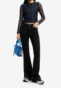 Jeans neri a zampa d'elefante abbinati a un top in rete blu attillato a maniche lunghe con un motivo circolare. Accessoriato con una borsa blu.
