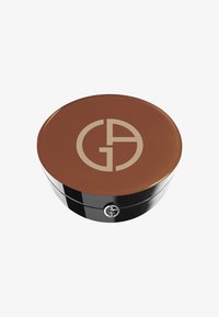 Compacto redondo con una crema marrón oscura en el interior, con una superficie brillante y un logo dorado en la parte superior, y una base negra brillante.
