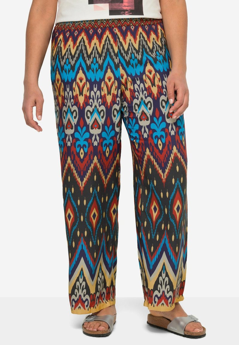 Luźne spodnie w wzory wykonane z lekkiej tkaniny, charakteryzujące się żywymi, geometrycznymi wzorami w kolorze czerwonym, niebieskim, żółtym i czarnym. Elastyczny pas.
