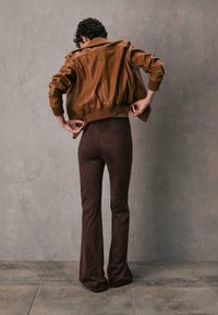 Braune Leder-Bomberjacke mit gerippten Bündchen, kombiniert mit dunkelbraunen, sich weitenden Hosen aus glattem, leichtem Stoff.