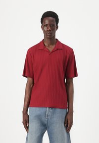 Rød kortærmet polo shirt med et tekstureret, ribbet design og en spids krave. Båret med lyseblå jeans.