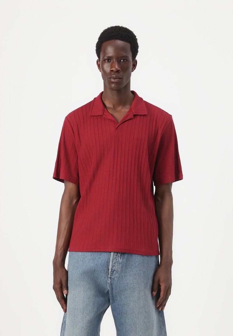 Rød kortærmet polo shirt med et tekstureret, ribbet design og en spids krave. Båret med lyseblå jeans.