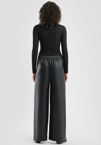 Czarny prążkowany top z długim rękawem, zestawiony z szerokimi, wysokim stanem spodniami z czarnej sztucznej skóry, posiadającymi elastyczny pas i gładką teksturę.