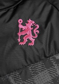 Tessuto nero con un motivo testurizzato sotto un prominente emblema di leone ricamato in rosa che tiene un bastone. Superficie liscia, design elegante.