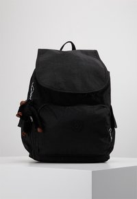 Mochila negra con cierre de solapa, bolsillo frontal y textura de tela. Presenta un pequeño accesorio de peluche sujeto por una cadena de plata.