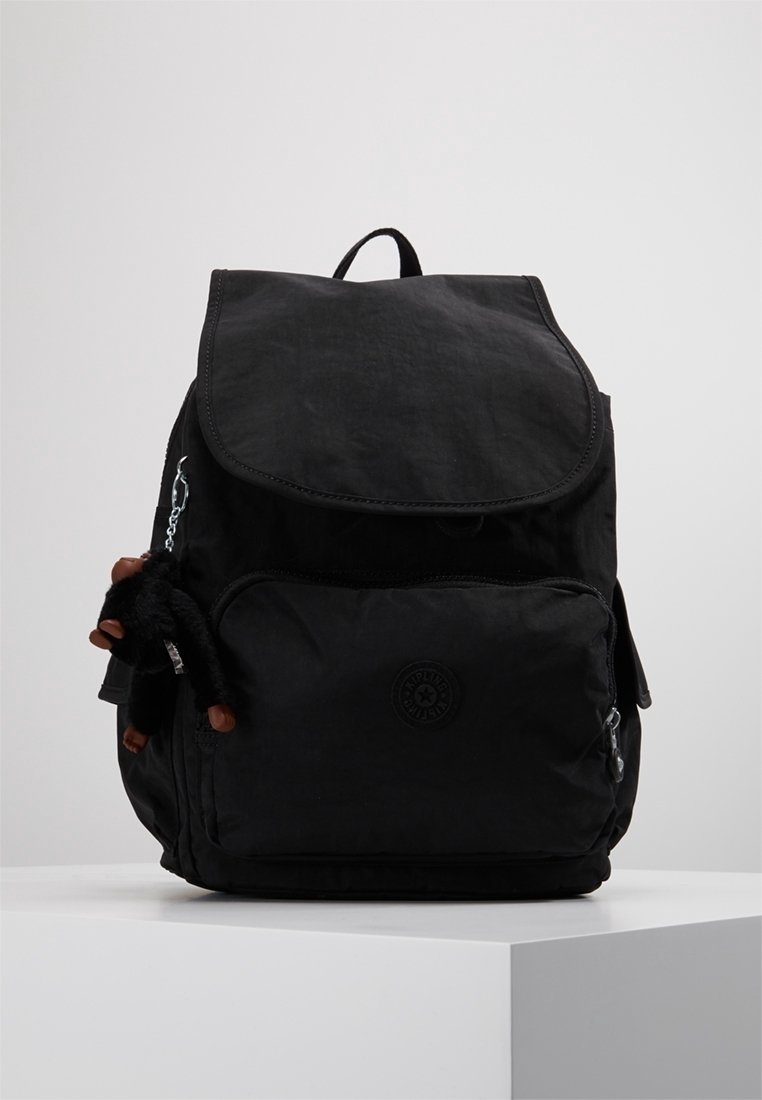 Mochila negra con cierre de solapa, bolsillo frontal y textura de tela. Presenta un pequeño accesorio de peluche sujeto por una cadena de plata.