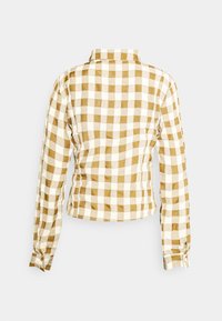 Camisa abotoada com padrão quadriculado em castanho e branco, mangas longas e colarinho. Apresenta uma silhueta ajustada com franzidos nas laterais.