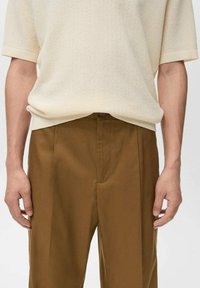 Pull en maille crème à manches courtes associé à un pantalon marron taille haute. Le pull présente un tissage texturé et des poignets côtelés.