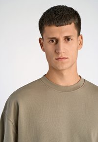 Felpa khaki con collo rotondo a coste e vestibilità rilassata. Tessuto liscio e design minimalista, con un sottile motivo orizzontale.