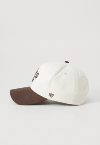 Baseballcap med en hvid stofkrone og en brun skygge. Har broderet tekst på fronten og et logo på siden.