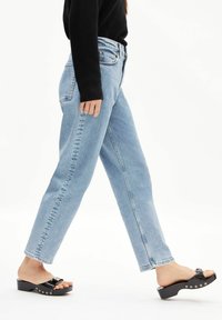 Lichtblauwe jeans met hoge taille en een rechte pijp. Draag ze met zwarte slip-on sandalen met een glanzende afwerking en decoratieve hardware.