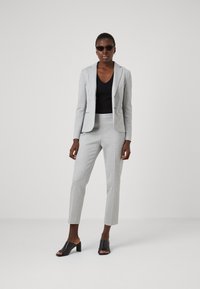 Svetlo sivi prirezan kostim z enorednim blejzerjem in ožjimi hlačami, v kombinaciji s črno bluzo in črnimi natikači na debelem petu.