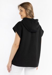 Zwarte hoodie met korte mouwen, met een ruime pasvorm, zachte textuur en een eenvoudig ontwerp, voorzien van een capuchon en zonder verdere versieringen.
