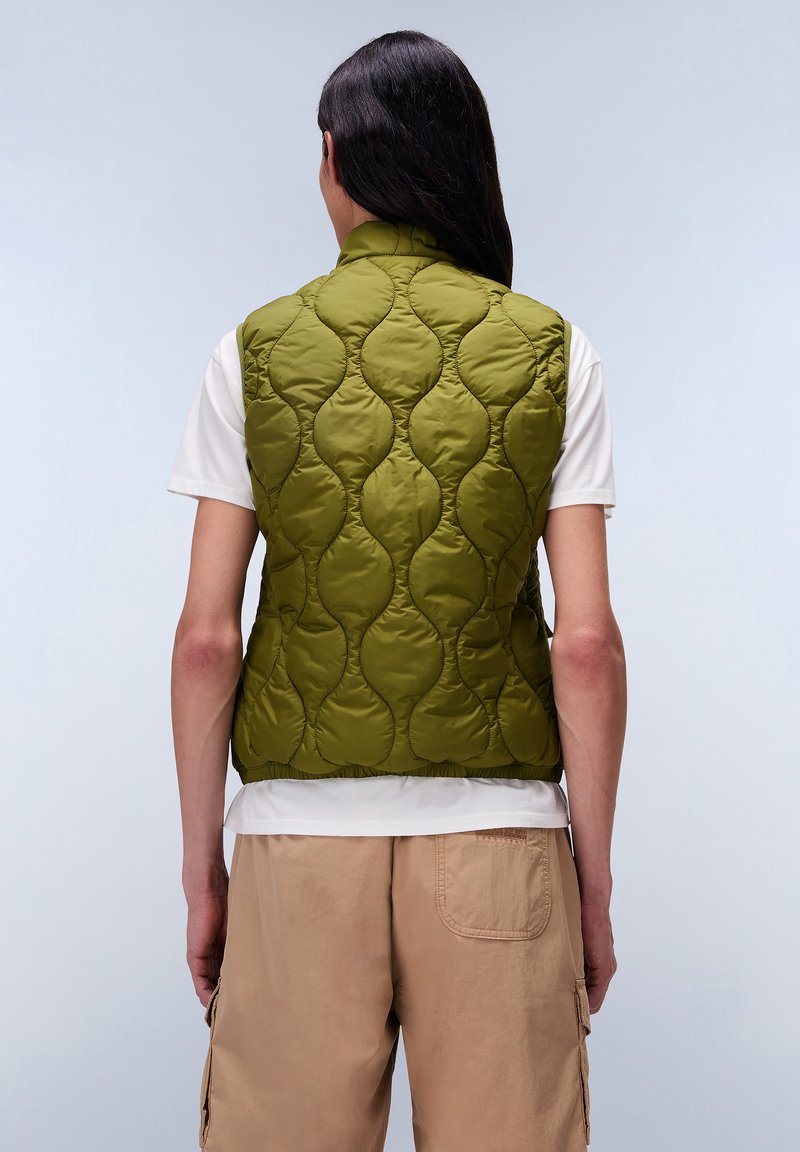 Oliwkowa pikowana kamizelka z falistym wzorem, lekki materiał, wysoki kołnierz i elastyczny dół, nałożona na białą koszulkę.