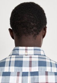 Koszula krótki rękaw, z kołnierzykiem w niebiesko-białą-czerwoną kratę. Posiada guzik z tyłu kołnierza oraz prosty krój.