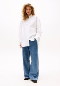 Camicia bianca in cotone con bottoni e una tasca sul petto, abbinata a jeans a gamba larga in denim blu chiaro e dalla vestibilità comoda.