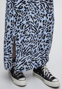 Ljusblå maxiklänning med svart djurmönster, med en sidoklyvning. Matchas med svarta hög- och låga sneakers med vita gummisulor.