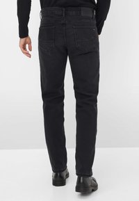 Jeans in denim neri con una vestibilità dritta, dotati di due tasche posteriori, dettagli cuciti e una superficie liscia. Indossati con calzature nere.