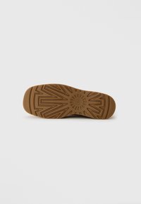Semelle de chaussure en caoutchouc marron avec un motif de bande de roulement géométrique et un logo circulaire au centre sur un fond gris uni.