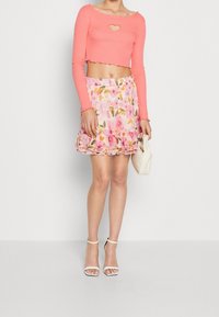 Rosa croptop med hjärthål, kombinerad med en blommig minikjol med volangkant. Vita högklackade sandaler och clutch.