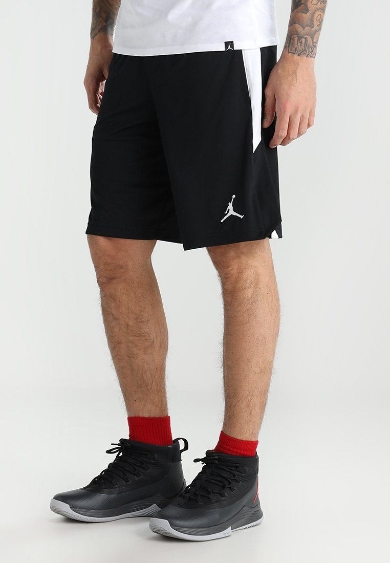 Man som bär svarta Jordan-basketshorts, röda strumpor och svarta högskor, står mot en neutral bakgrund.