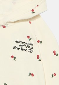Helle Creme-Hoodie mit Kirschdruck, ausgestattet mit einer Kordelzugkapuze und gesticktem "Abercrombie and Fitch New York City" auf der Vorderseite.