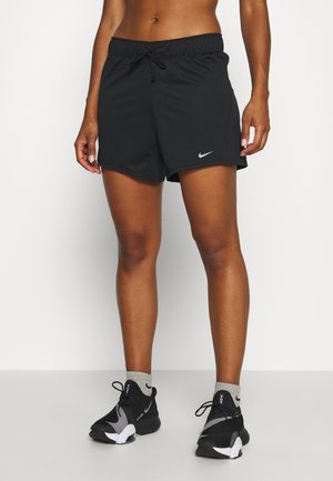 Osoba nosząca czarne sportowe spodenki Nike ze sznurkiem, szare skarpetki Nike i czarno-białe buty do biegania Nike, stojąca na białym tle.