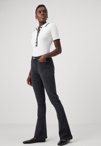 Polo shirt bianco a costine con bordi neri, abbinato a pantaloni a zampa d'elefante grigi scuri e ballerine nere. L'outfit presenta dettagli dei bottoni discreti.
