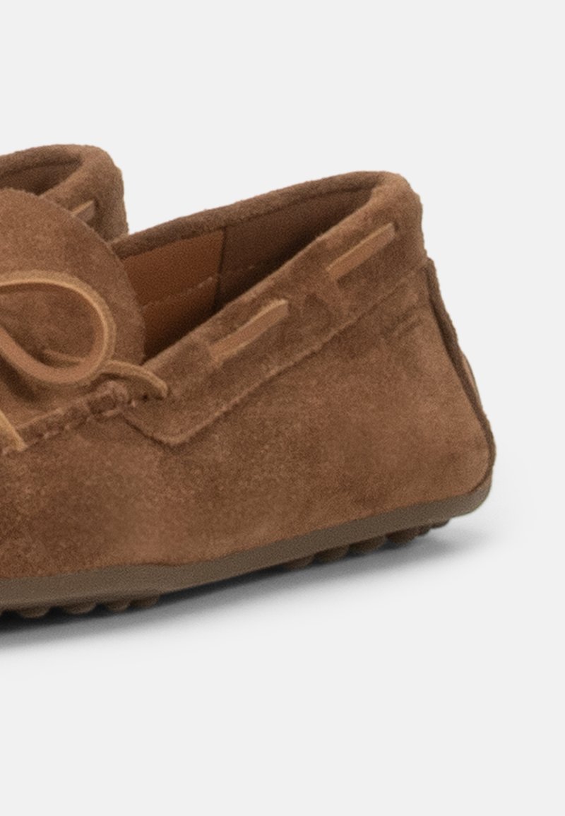 Bruine suèden mocassins loafer met rubberen zool en leren veterdetail op een witte achtergrond.