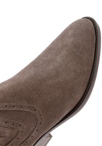Zapato de ante marrón con punta afilada, detalles perforados y suela lisa. El tacón está sutilmente contorneado y tiene un acabado brillante.