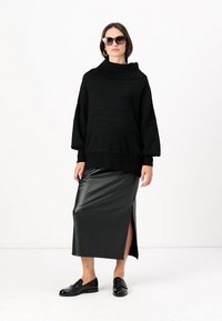 Un pull noir surdimensionné avec un col roulé côtelé, associé à une jupe en faux cuir noir élégante avec une fente haute sur la cuisse et des mocassins noirs.