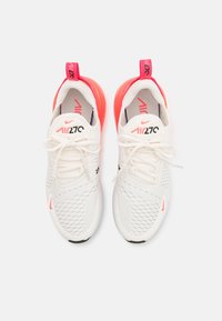 White athletic shoes with mesh upper, padded heel, and pink accents. Features traditional laces and prominent branding on the tongue and heel.