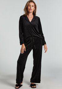 Mustapukuiset pyjamapuku pehmeästä kankaasta, johon kuuluu napitettava paita ja naruhelmaiset löysät housut. Housuissa on käännetyt lahkeet.