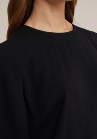 Černý top s kulatým výstřihem, vyrobený z texturované látky. Látka vypadá lehce, s jemnými zvrásněnými detaily a volánovými rukávy.