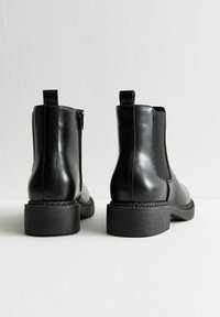 Botines de cuero negro con una textura suave, paneles laterales elásticos, punta redonda y un pequeño tacón cuadrado, que cuentan con una lengüeta en la parte trasera.