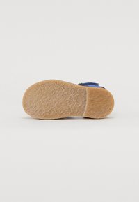 Blå mockaskor med en beige texturerad gummisula. Har ett justerbart band och en slät ovansida.