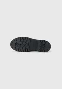 Semelle de chaussure en caoutchouc noir avec un profond motif de rainure pour un meilleur grip, affichant un logo de marque visible et des éléments de design symétriques.