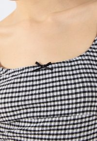 Black and white checked fabric with gathered texture, featuring a small black bow accent at the neckline of a sundress.