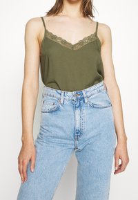 Olive green camisole with lace trim at neckline, paired with high-waisted light blue denim shorts featuring a classic five-pocket design.