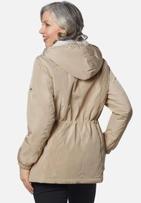 Beige gewatteerde jas met een capuchon, strikband in de taille en elastische manchetten. Gladde stof met een subtiele glans en geen zichtbare patronen.