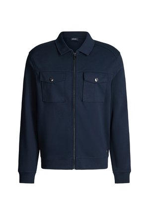 Marineblauwe jas met ritssluiting gemaakt van een katoenmengsel met twee borstzakken, drukknopen en geribbelde manchetten. Gladde textuur en gestructureerd kraagontwerp.