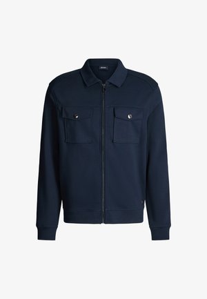 Granatowa bluza zapinana na zamek wykonana z bawełnianej mieszanki z dwoma kieszeniami na piersi, zatrzaskami i ściągaczami na rękawach. Gładka faktura i usztywniony kołnierz.