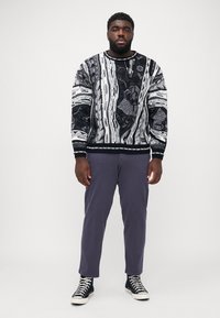 Knit black and white sweater with abstract patterns, paired with purple pants and black high-top sneakers featuring white laces.