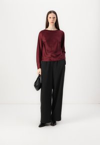 Burgundy satin long-sleeve top paired with high-waisted, wide-leg black trousers and a small black handbag, against a plain background.