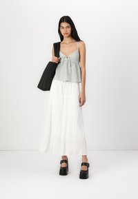 Haut sans manches à carreaux gris clair avec un détail de nœud, associé à une jupe maxi blanche à volants et des chaussures à plateforme noires. Sac fourre-tout noir.