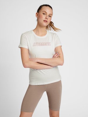 Hvid kortærmet t-shirt med "HUMMEL" trykt i pink, parret med lysebrune tætsiddende shorts. Stofferne ser bløde og afslappede ud.