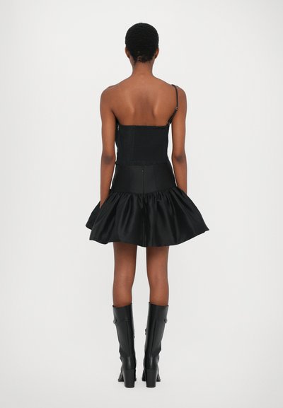 Vestido negro con un torso ajustado y una falda acampanada. Con tirantes finos ajustables y un respaldo texturizado. Llevado con botas negras hasta la rodilla.